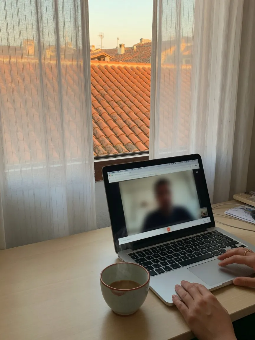 Sesión de psicología online: portátil junto a la ventana, en pantalla una silueta desenfocada, manos en el teclado.